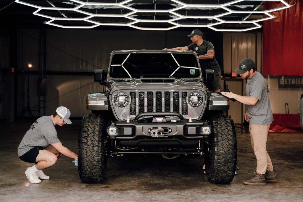 Three men are working on a jeep in a garage.