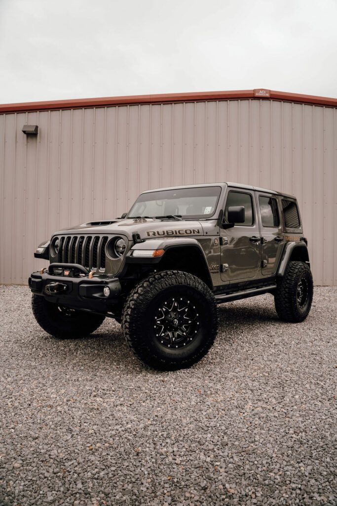 A jeep wrangler is parked in a gravel lot in front of a building.