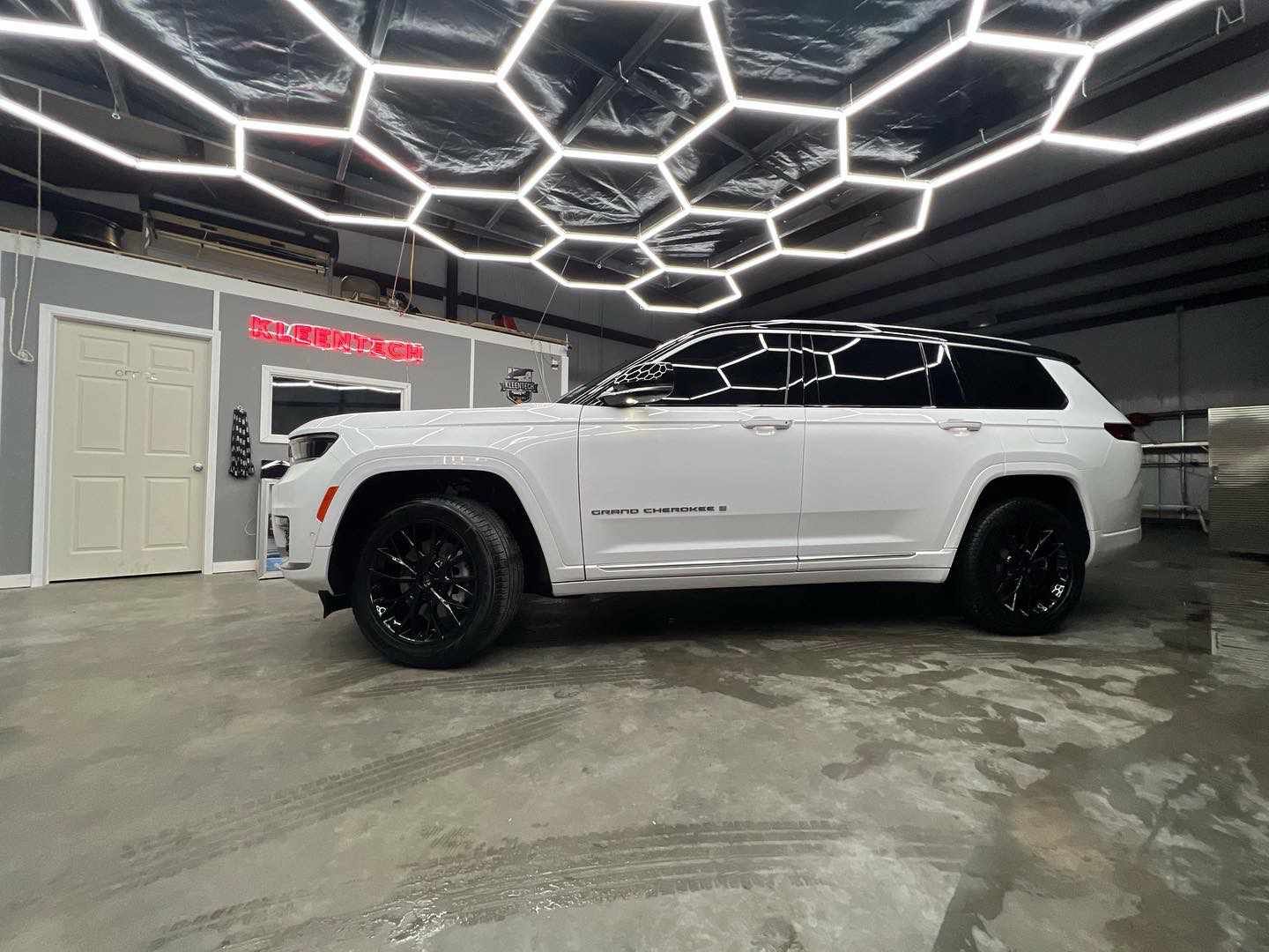 A white jeep grand cherokee is parked in a garage under a honeycomb ceiling.