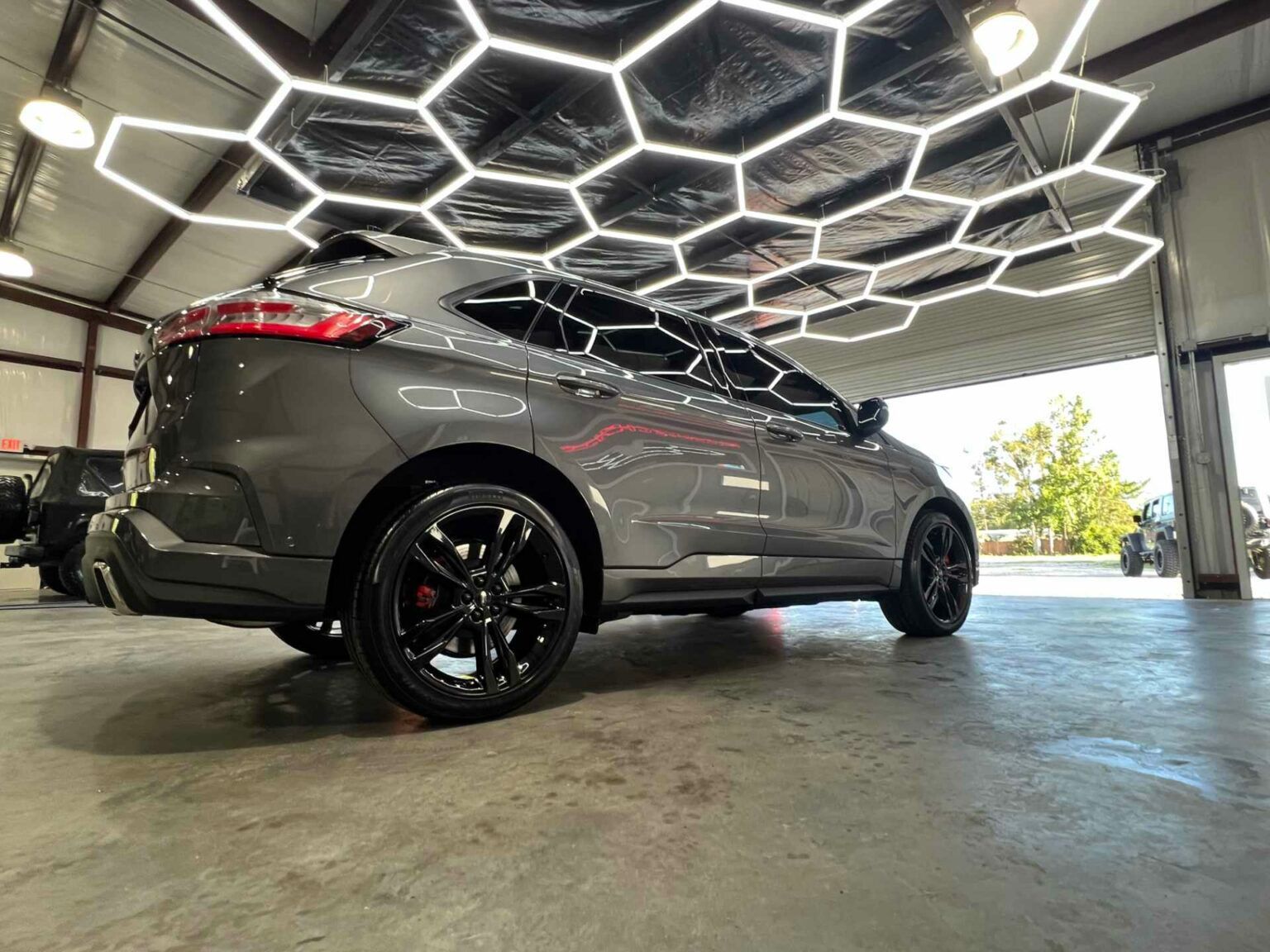 A gray car is parked in a garage under a honeycomb ceiling.