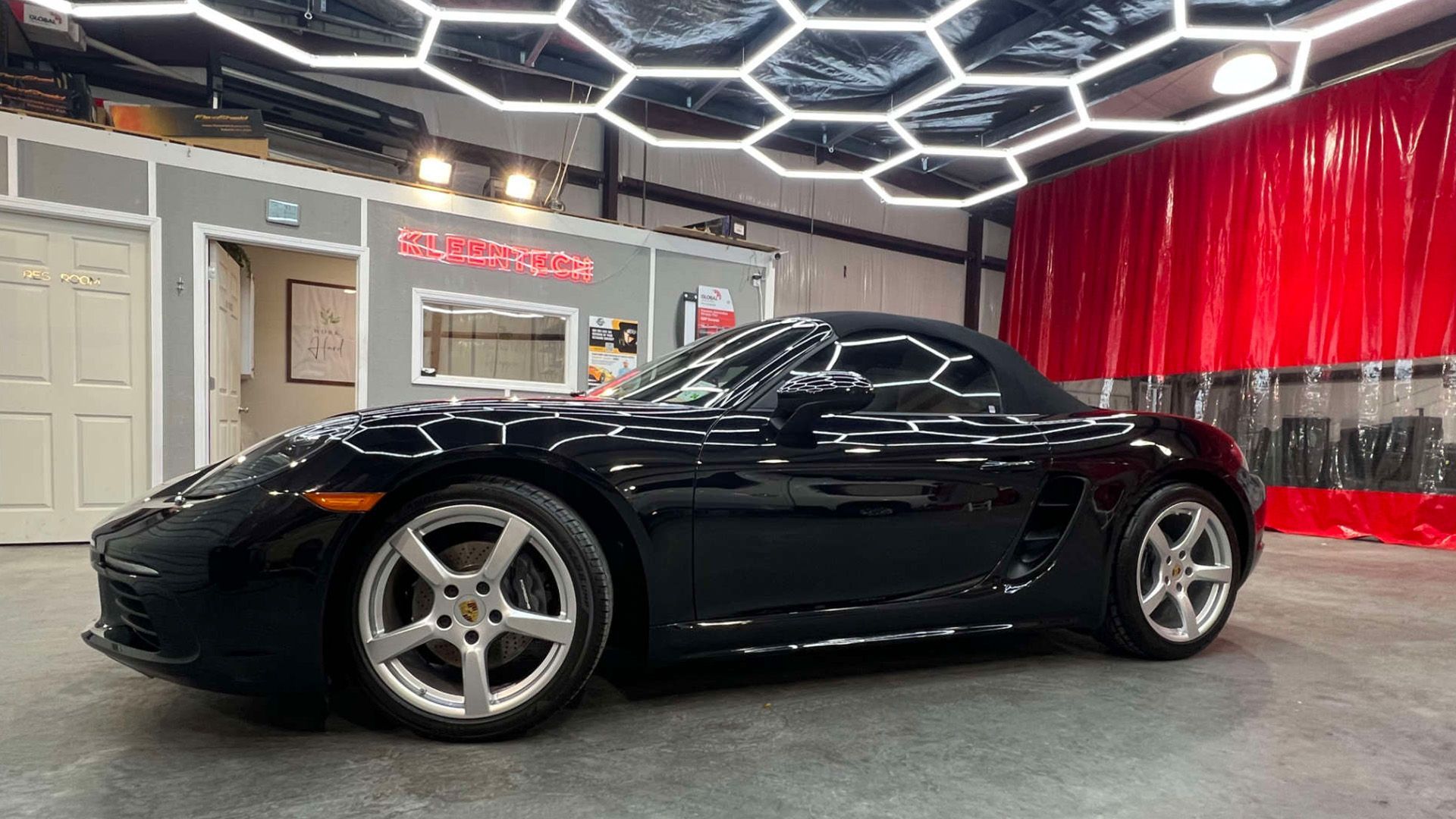 A black sports car is parked in a garage under a honeycomb ceiling.