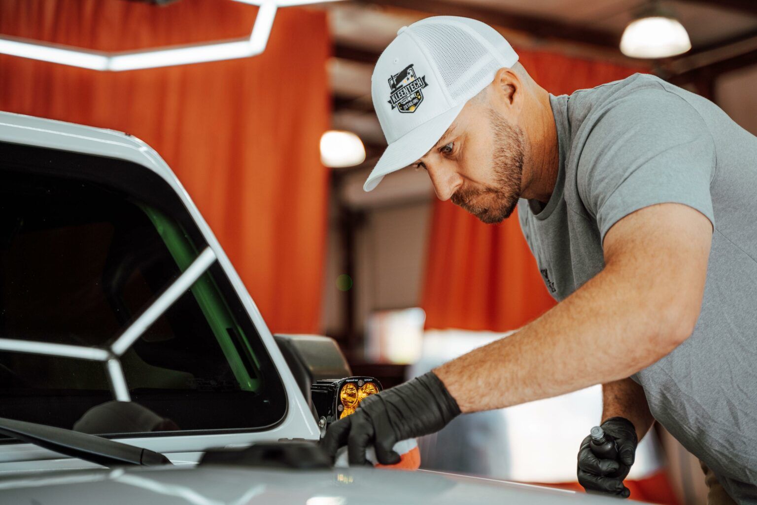 A man is working on the hood of a car in a garage.