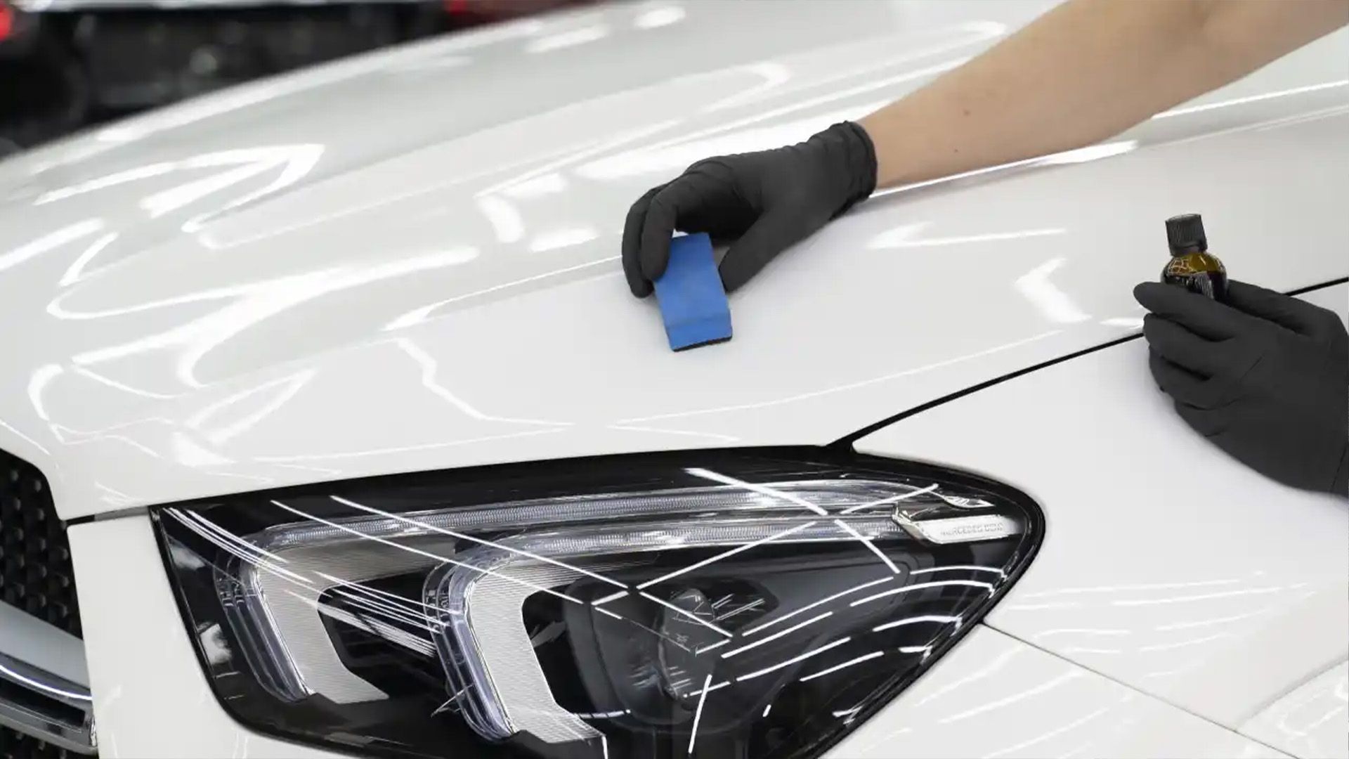 A person is polishing the hood of a white car.