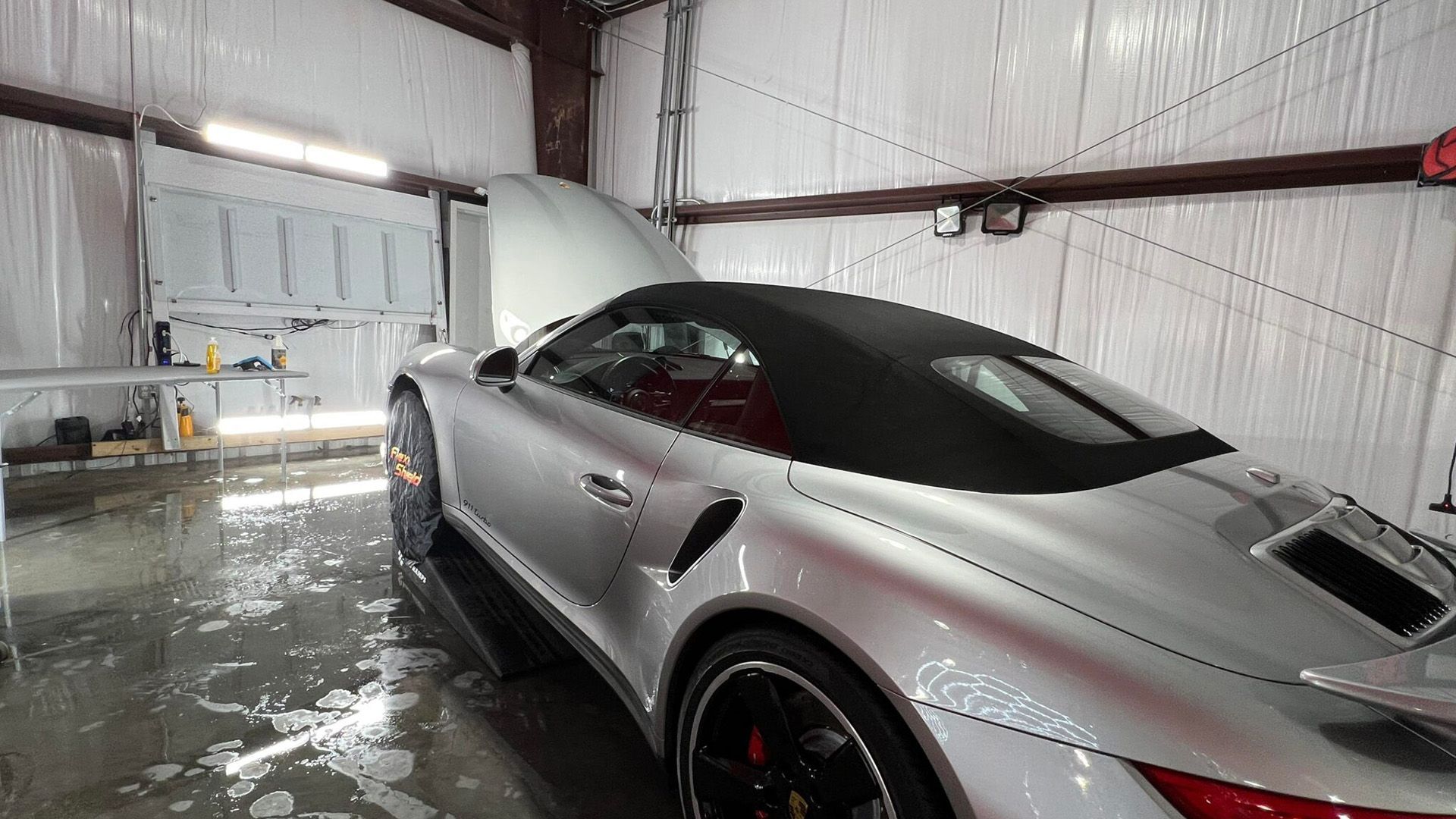 A silver sports car is parked in a garage with the hood up.