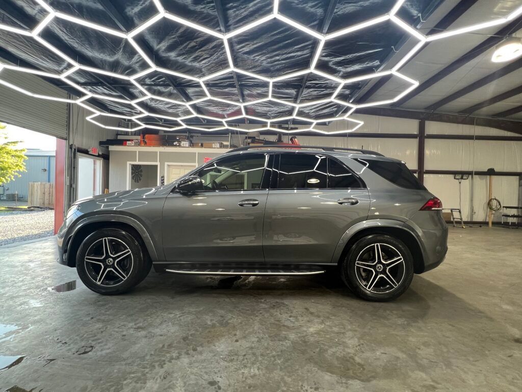 A gray suv is parked in a garage under a honeycomb ceiling.