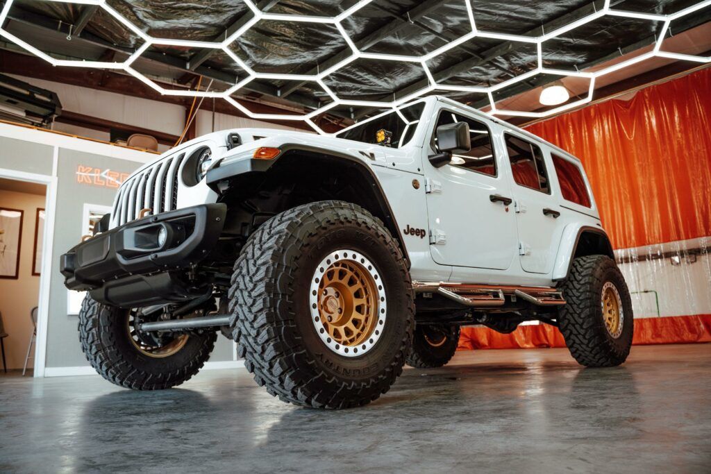 A white jeep with gold wheels is parked in a garage.