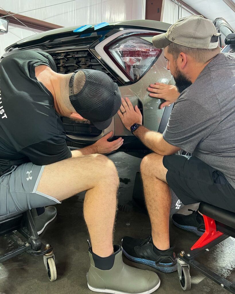 Two men are working on a car in a garage.