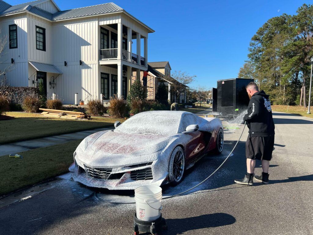 A man is washing a red sports car with foam.