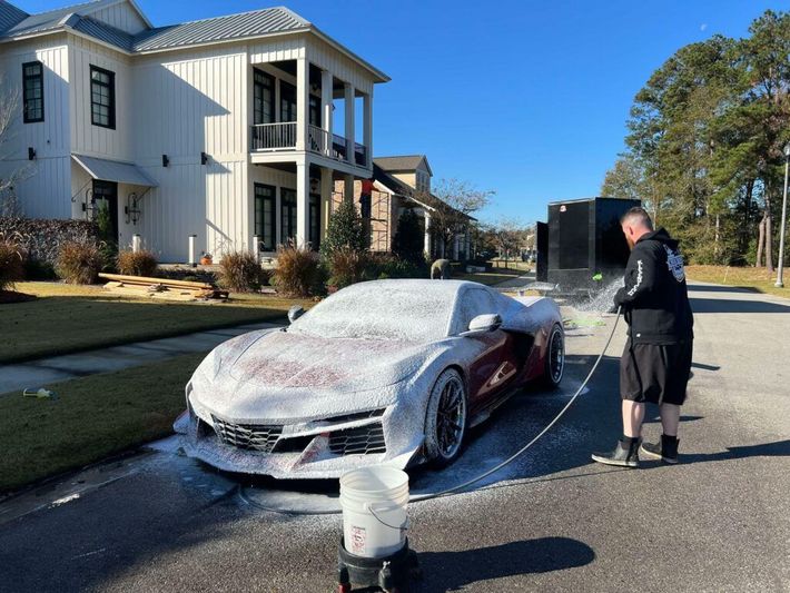 A man is washing a red sports car with foam.