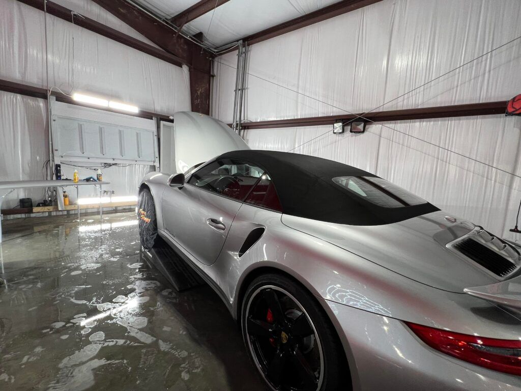 A silver sports car is parked in a garage with the hood up.