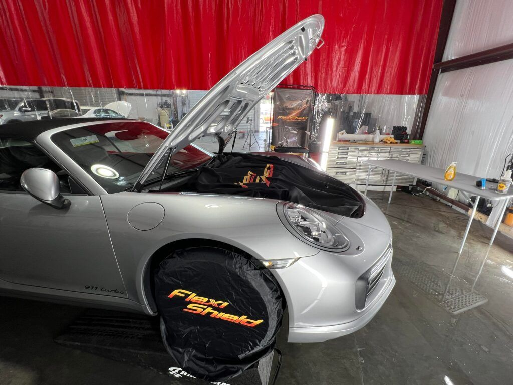 A silver porsche 911 cabriolet with its hood up in a garage.