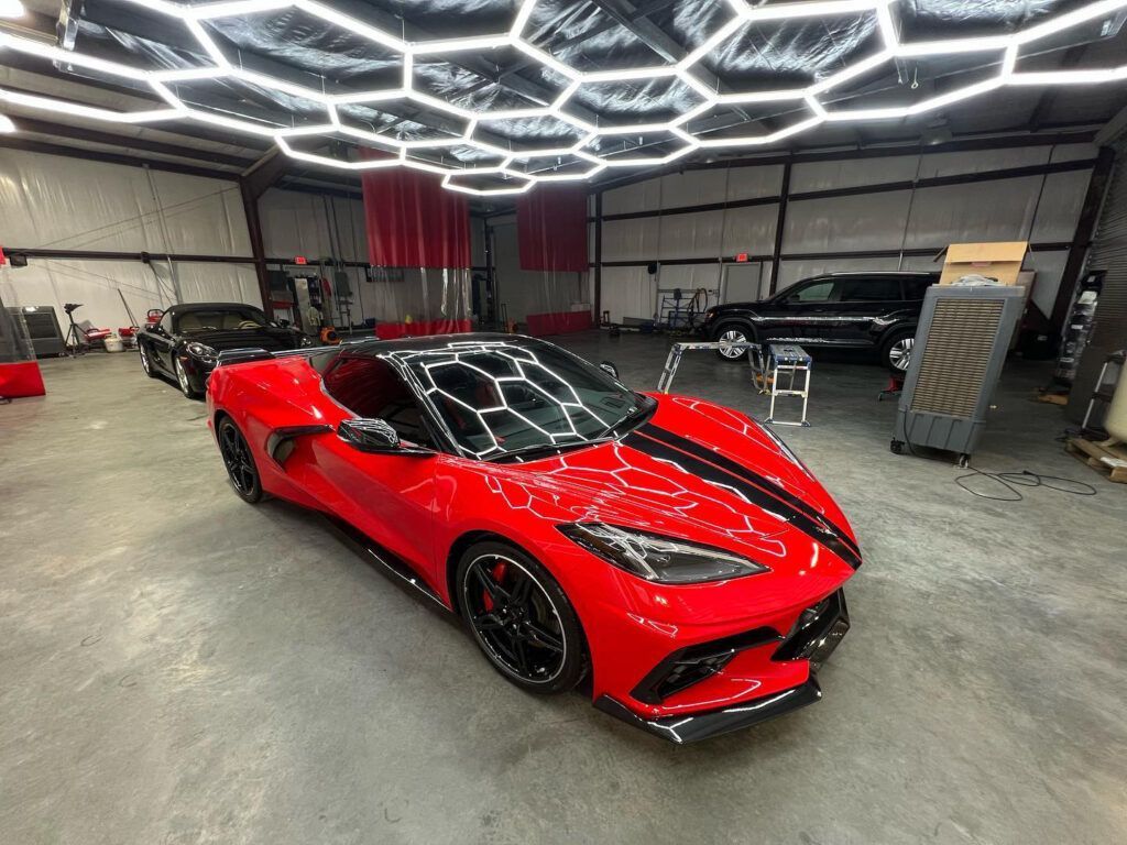 A red sports car is parked in a garage under a honeycomb ceiling.