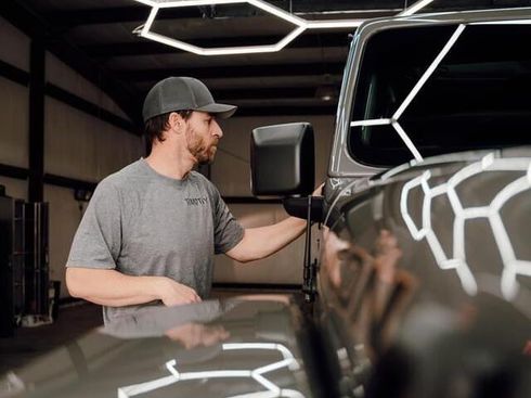 A man is adjusting the side mirror of a truck in a garage.