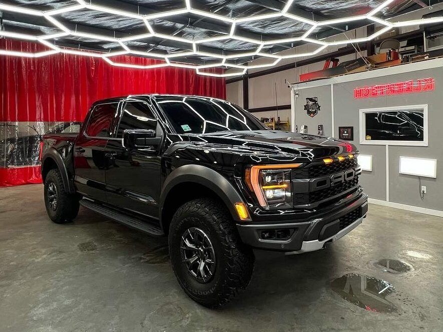 A black ford f150 raptor is parked in a garage.