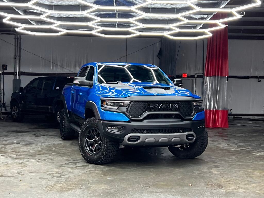 A blue ram truck is parked in a garage under a ceiling light.
