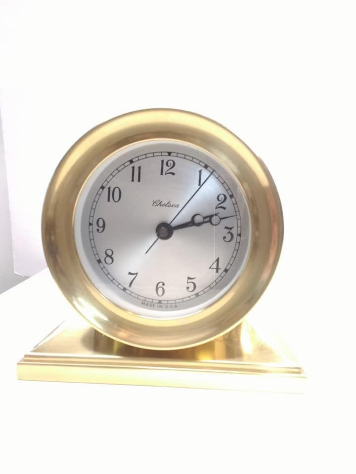Gold-toned desk clock. Round face with Roman numerals, hands at 2:10. Set on a rectangular base.