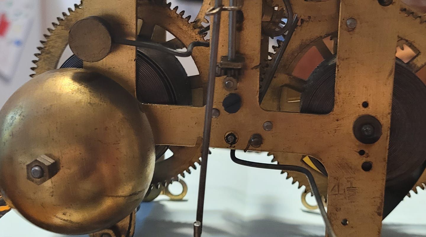 Clock mechanism, brass gears, circular bell, dark background, detailed view of internal parts.