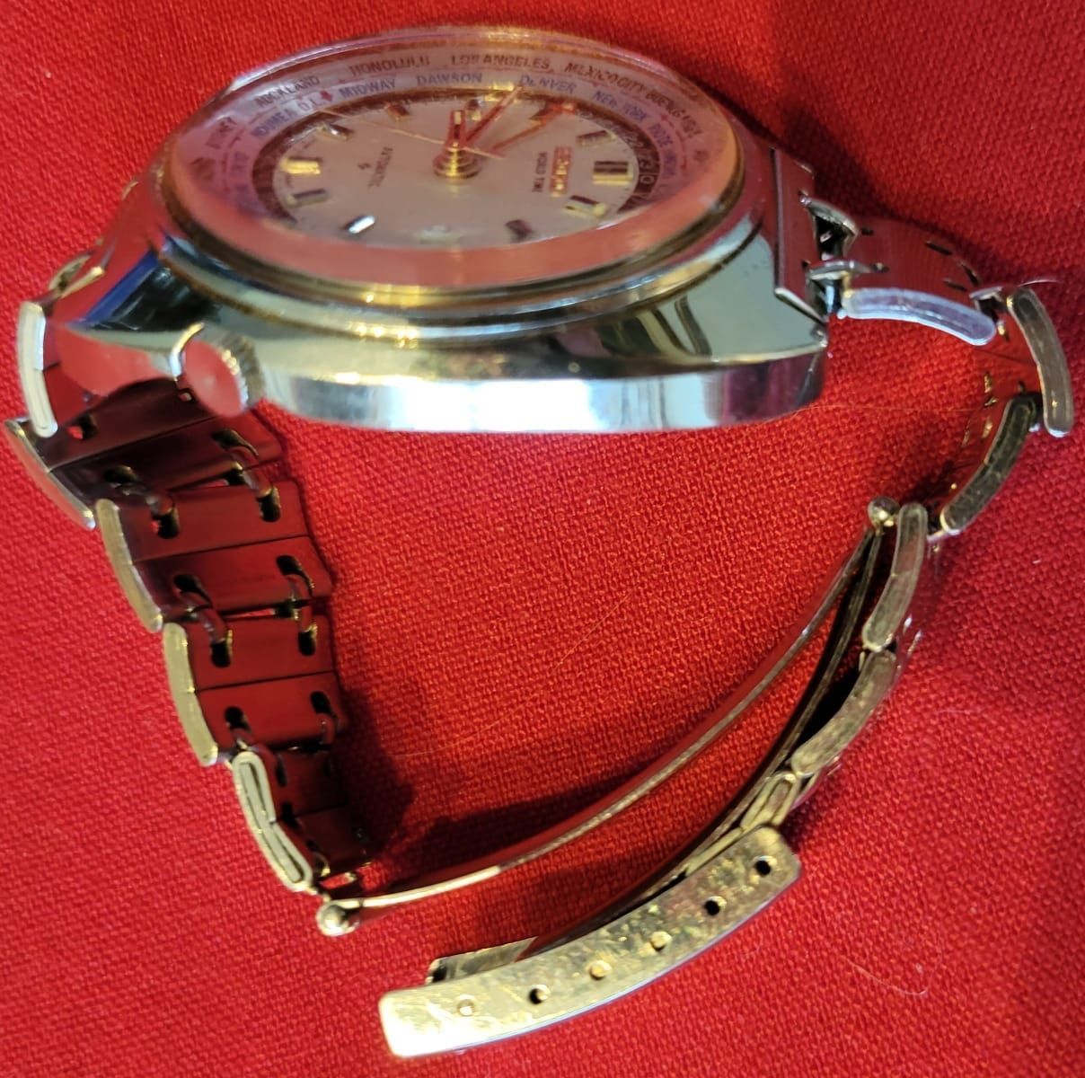Silver wristwatch with open metal band on a red surface.