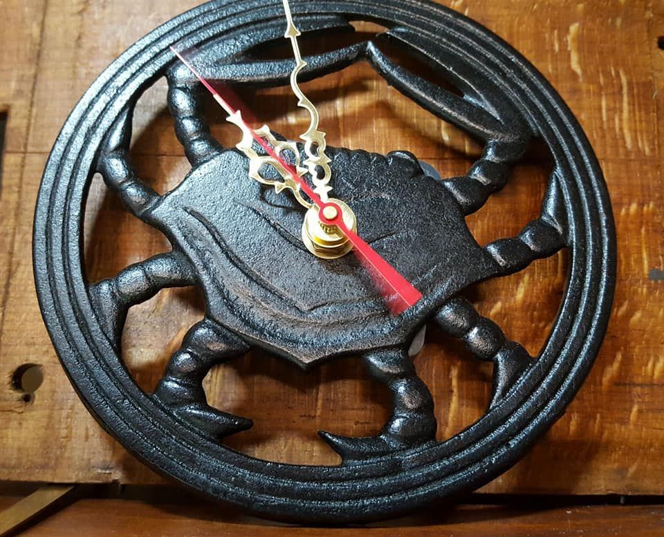 Black crab-shaped clock with red and gold hands, set on a wooden surface.