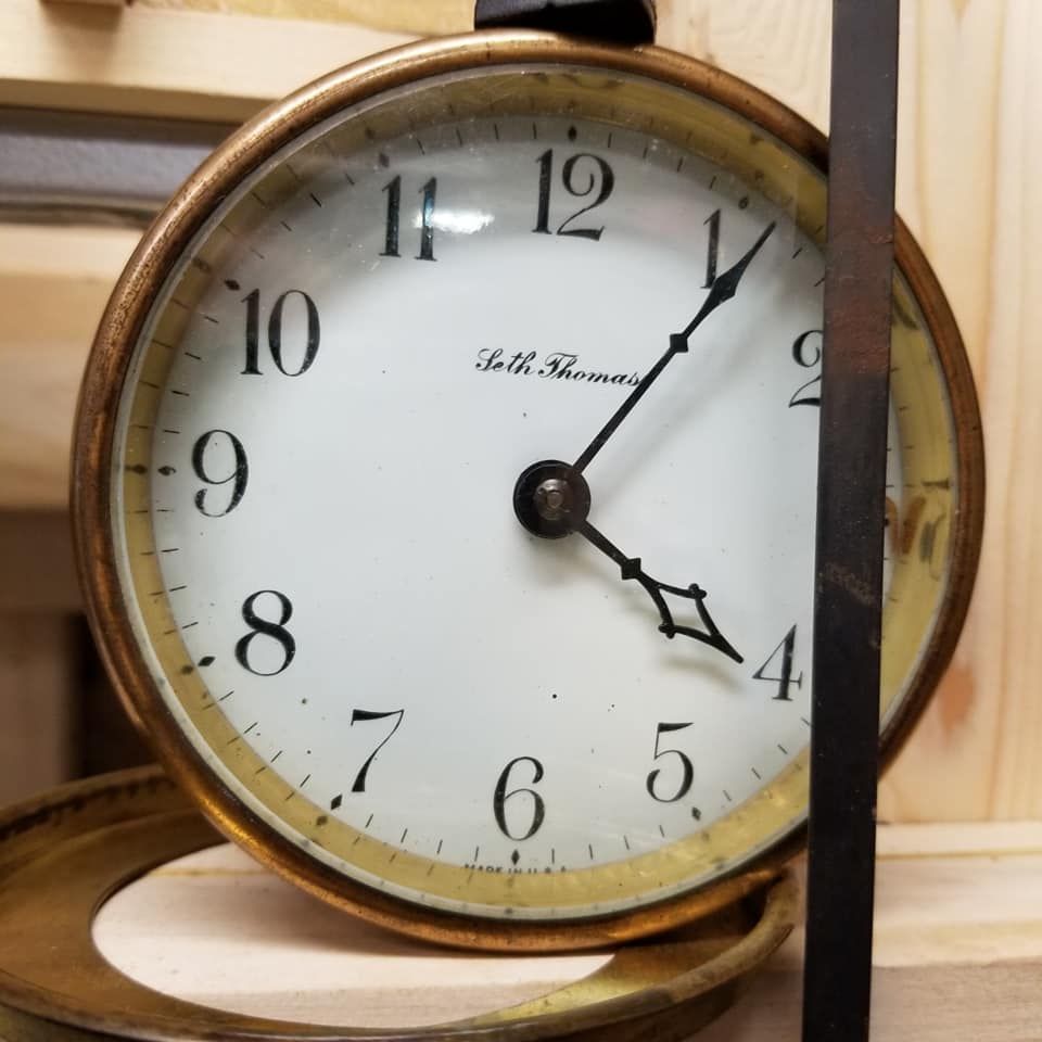 Round clock with a gold-toned frame, white face, and black hands pointing to 1:21.