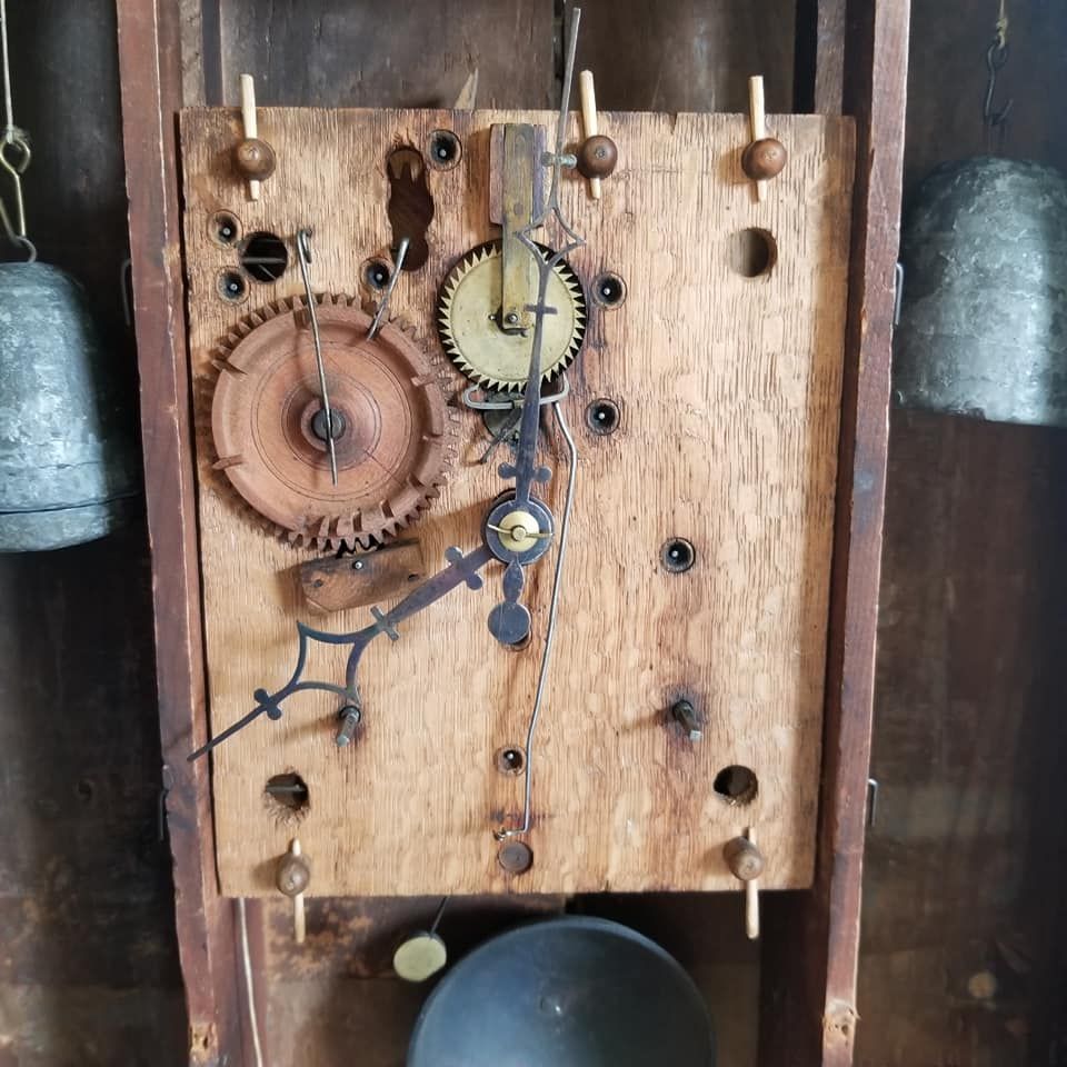 Clock mechanism with visible gears, hands, and bells. Wooden background.