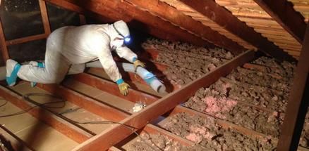 Skilled worker removing old attic mineral wool insulation during a renovation project.