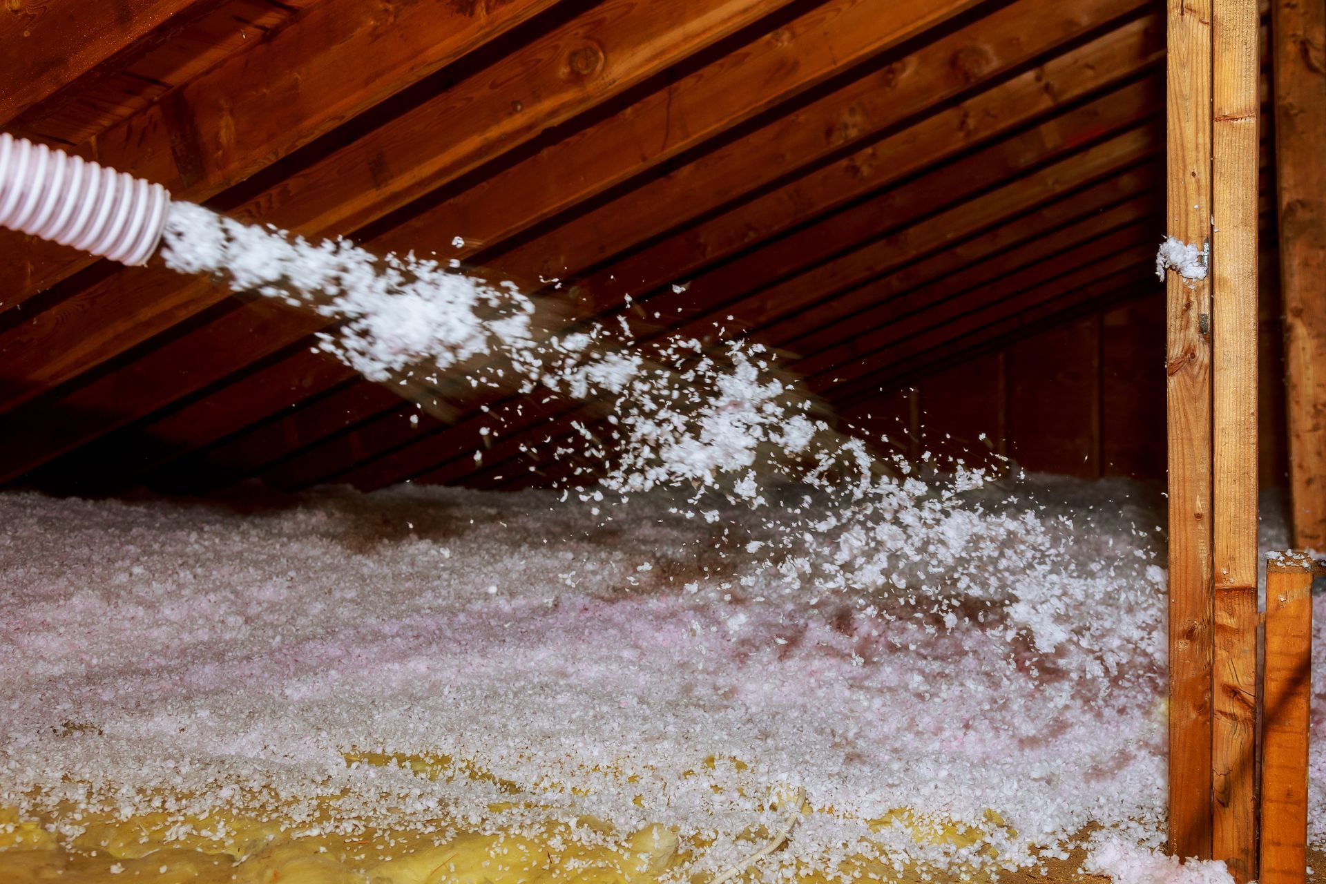 Worker using a spray nozzle to apply mineral rock wool insulation in a house attic.