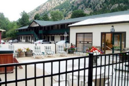 A fence surrounds a patio area with tables and chairs in front of a hotel.