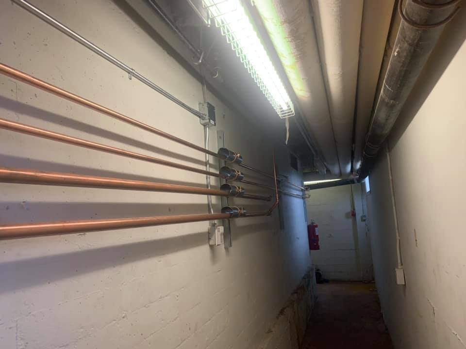 Un long couloir avec des tuyaux en cuivre suspendus aux murs.