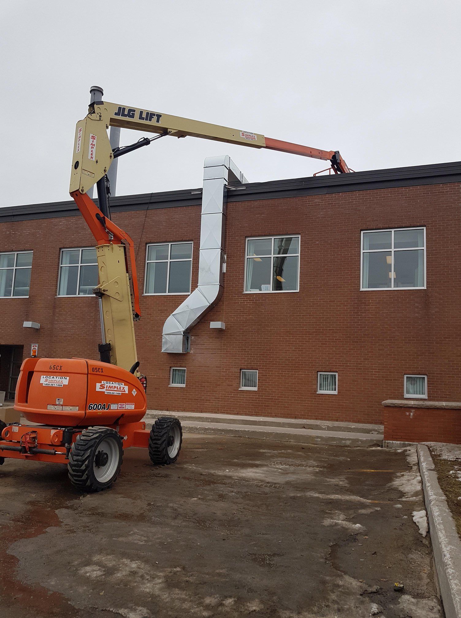 Un ascenseur JLG orange est garé devant un bâtiment en briques.