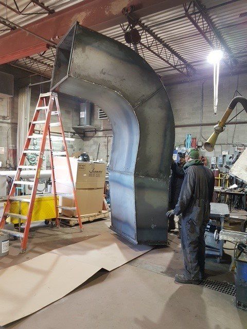 Un homme se tient debout à côté d'un gros tuyau métallique dans une usine.