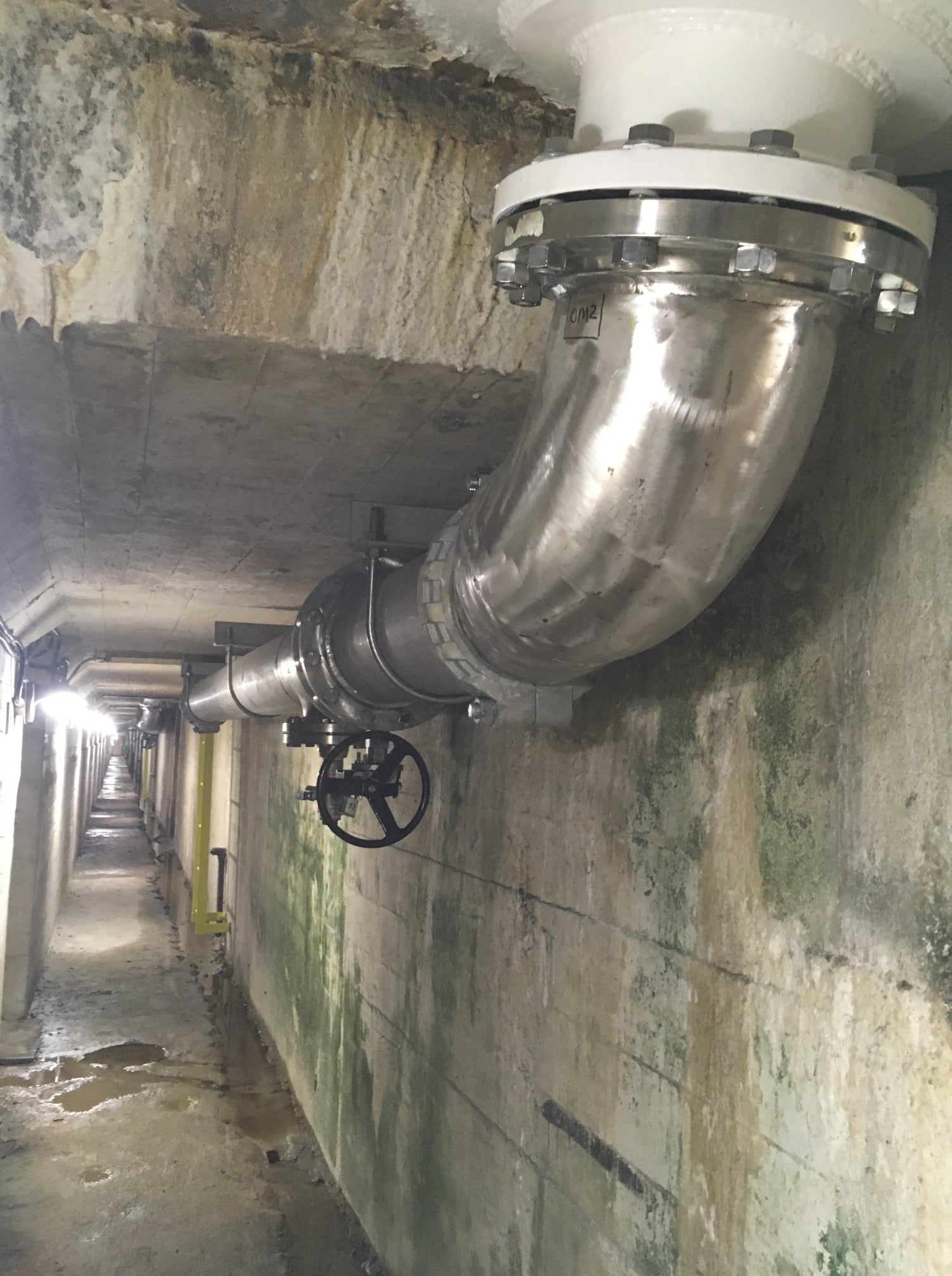 Un tuyau en acier inoxydable est suspendu à un mur en béton dans un tunnel.