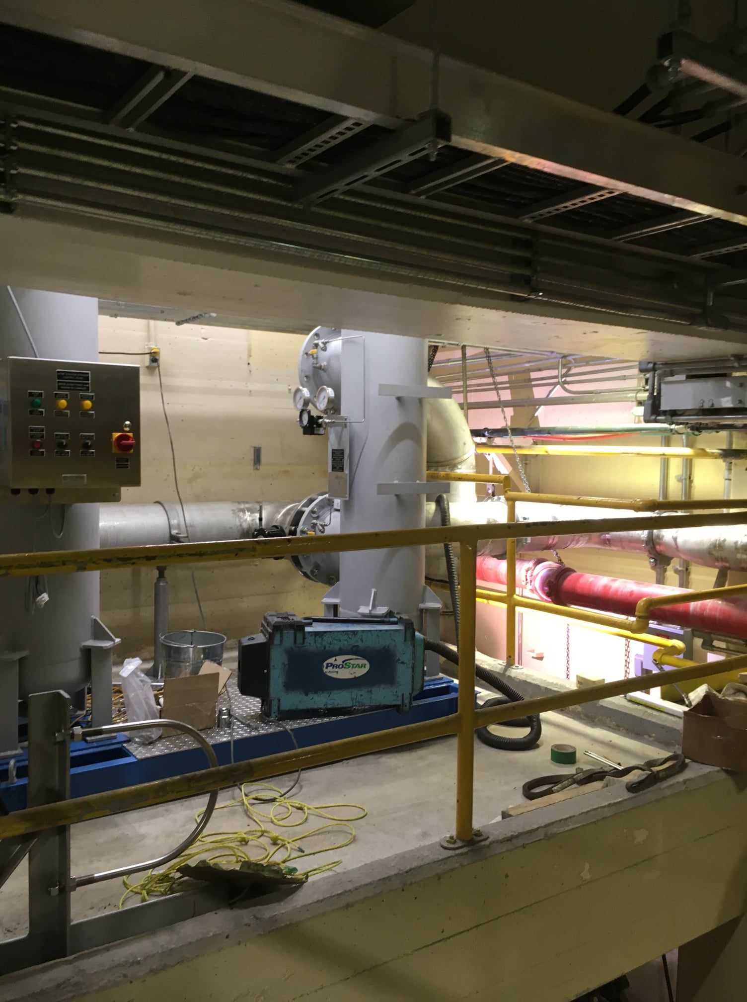 Une pièce avec beaucoup de tuyaux et une balustrade jaune.