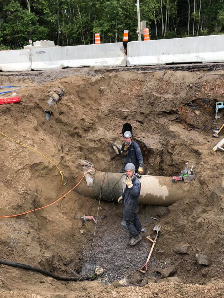 Deux hommes travaillent sur un gros tuyau dans la terre.