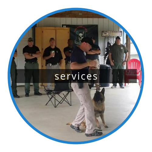Police K9 training indoors, handler with German shepherd; officers watch in background