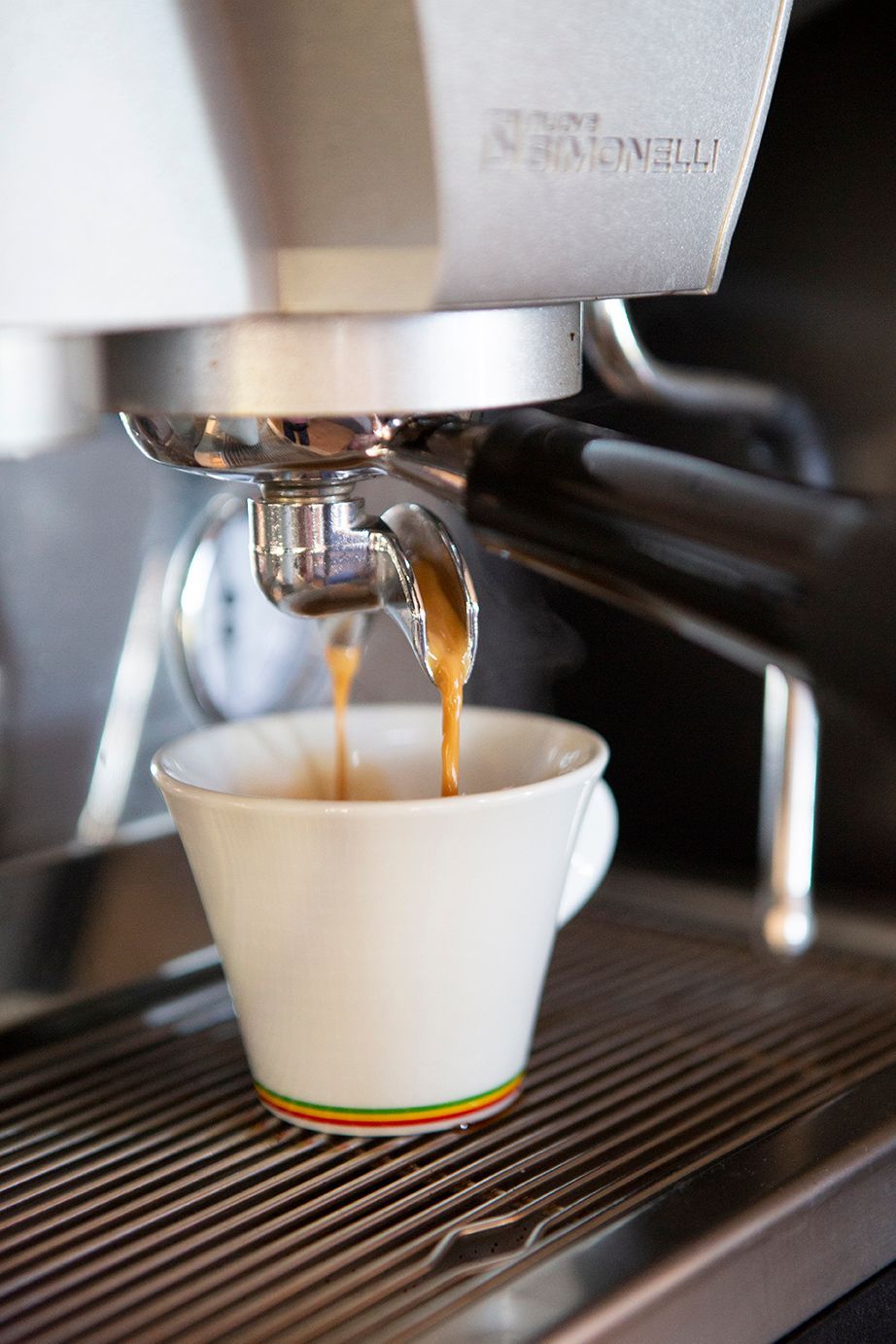 Máquina de café expreso que dispensa café en una taza blanca con una banda multicolor.
