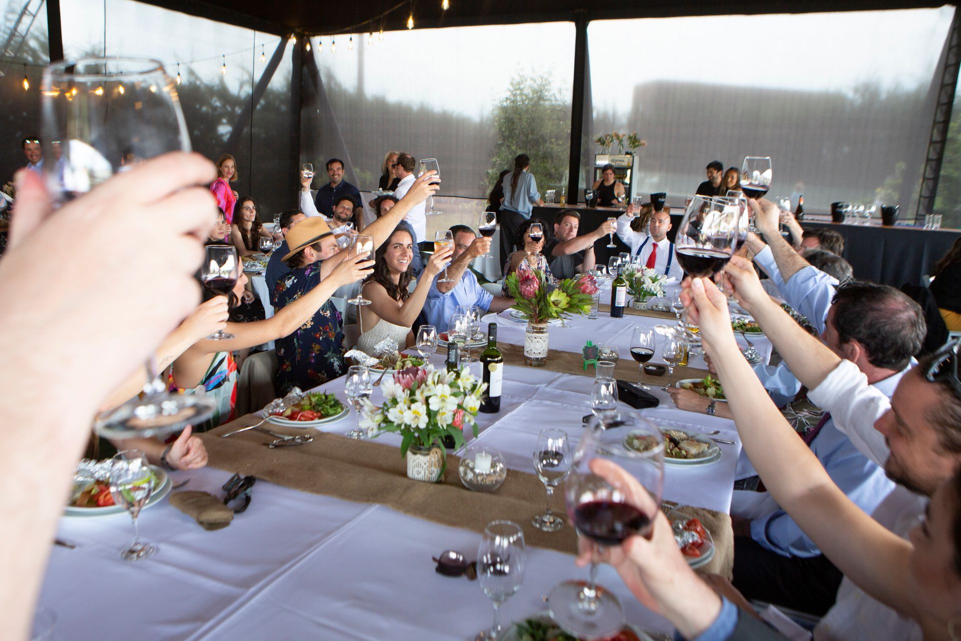 Una pareja se besa bajo un velo, sosteniendo un ramo. Edificio al fondo, día nublado.