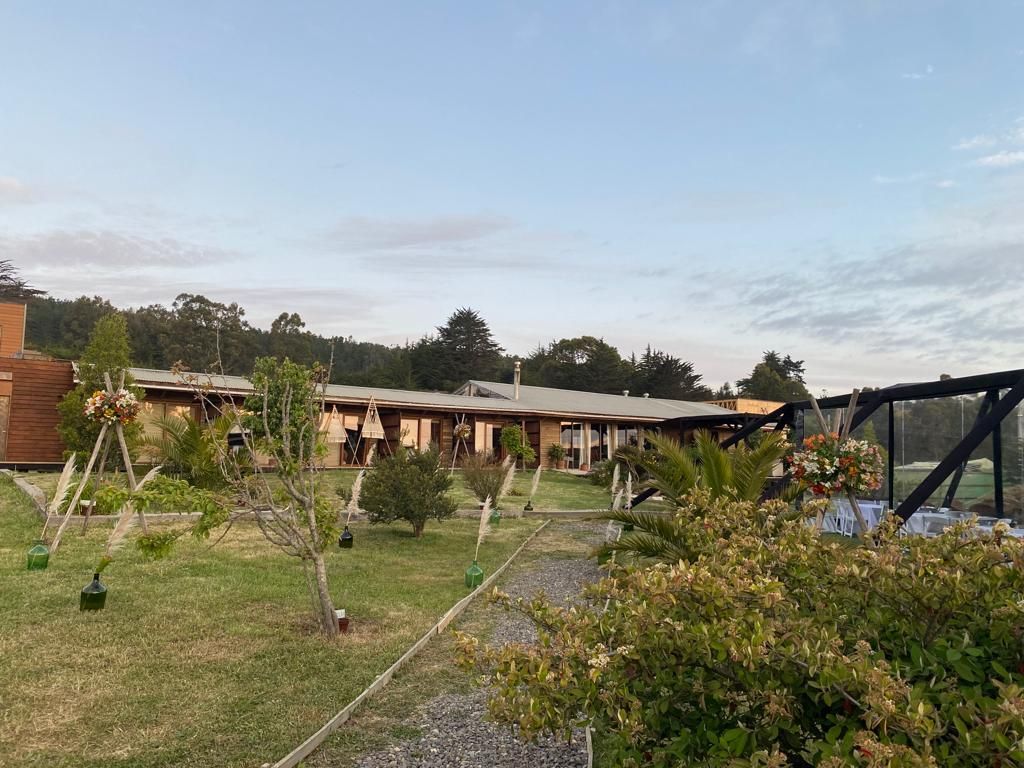 Un edificio largo y bajo con jardín. El césped y los arbustos verdes conducen a un patio con mesas y sillas.