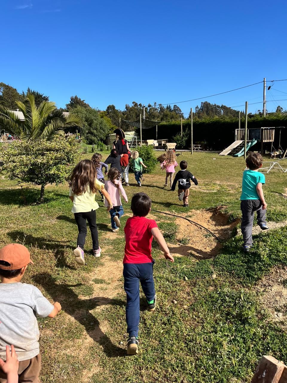 La gente se reunió en un porche, socializando cerca de un edificio blanco con plantas y un techo de vigas de madera.