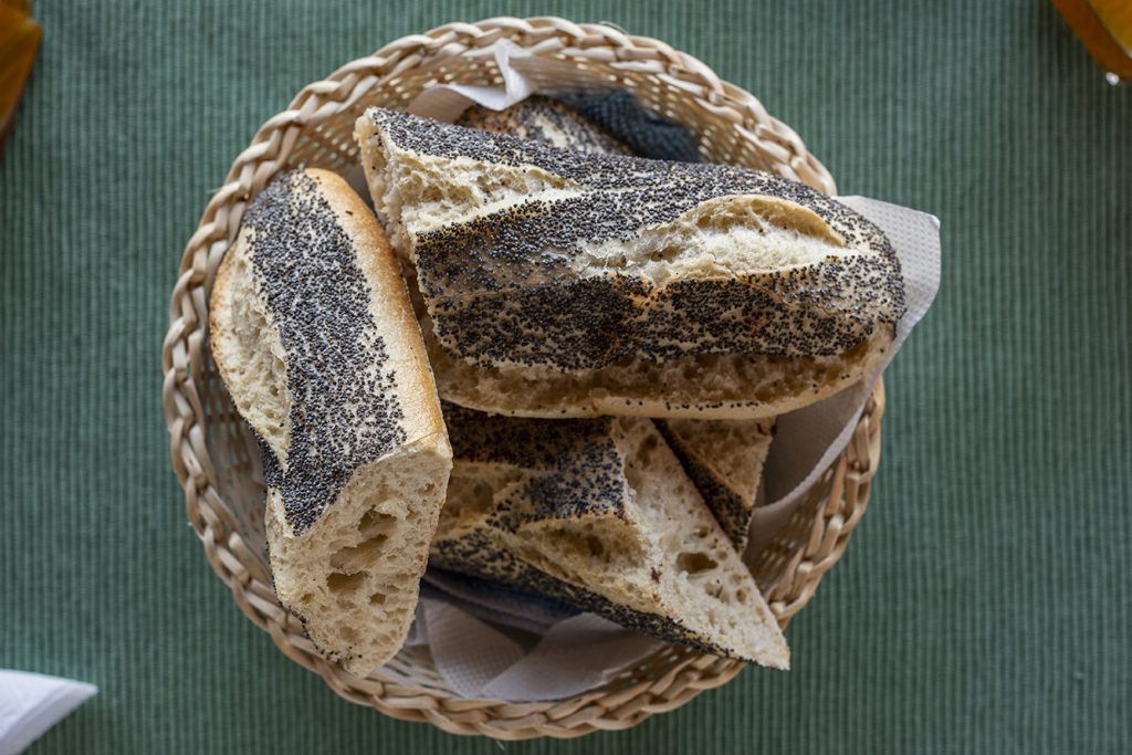 Rebanadas de pan con semillas de amapola en una cesta de mimbre sobre un mantel verde.