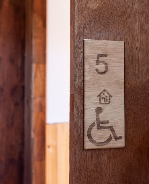 Puerta de madera con letrero: habitación número 5, símbolo de casa y símbolo de acceso para silla de ruedas.