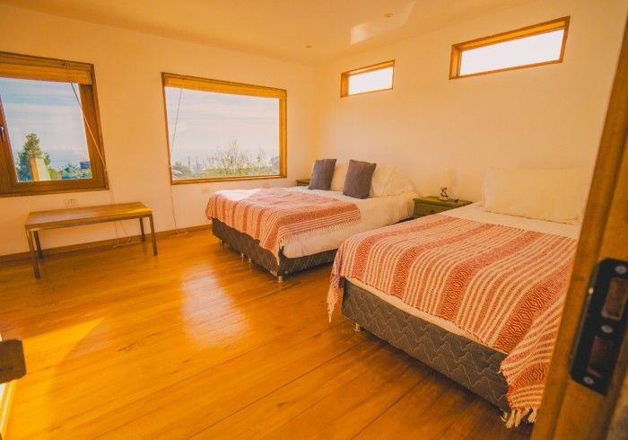 Dormitorio con dos camas, amplios ventanales, suelo y paredes de madera y luz natural.