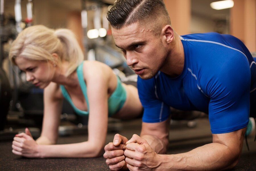A man and a woman are doing plank exercises in a gym.