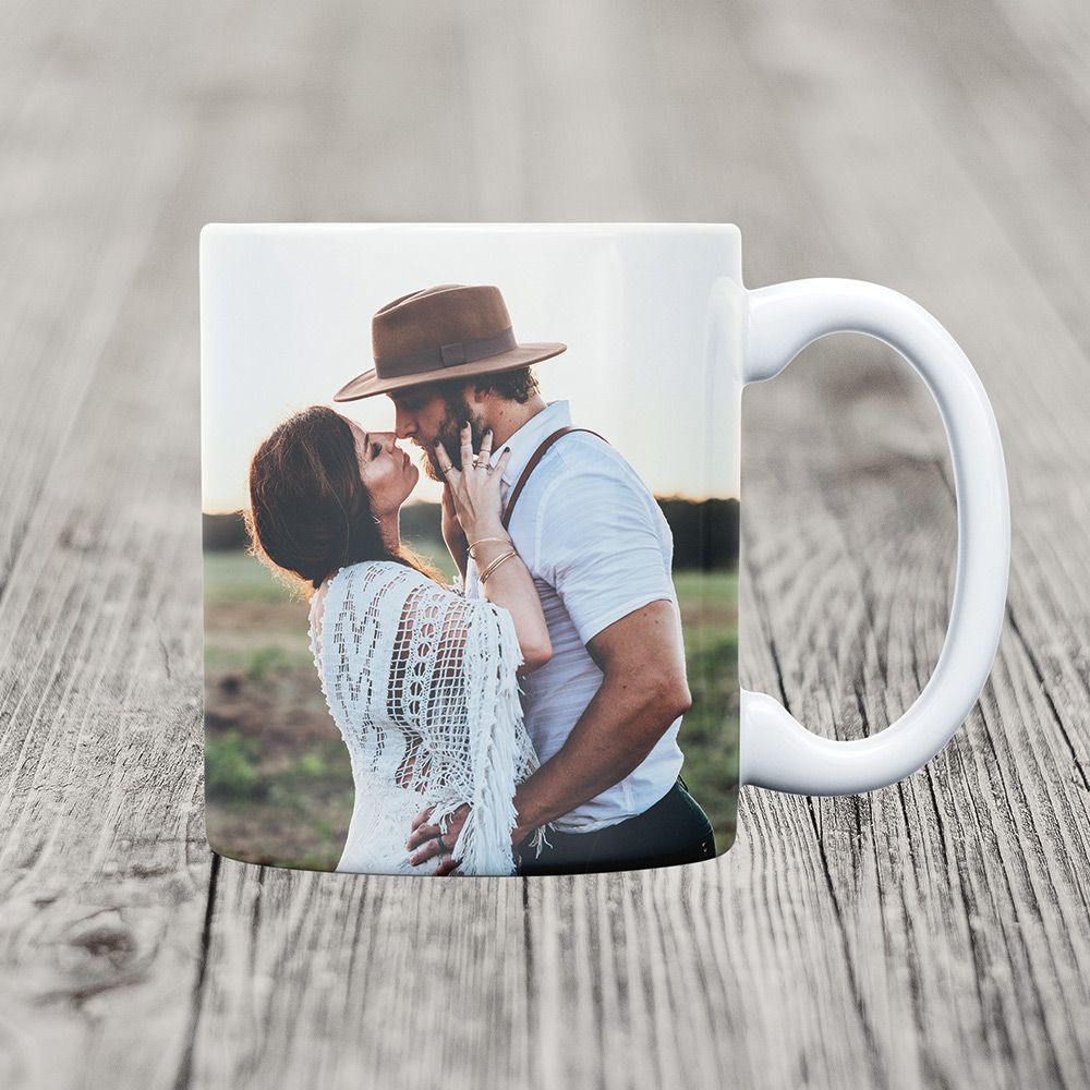 Mug with photo of couple about to kiss standing in a field. The mug is sitting on a wooden table