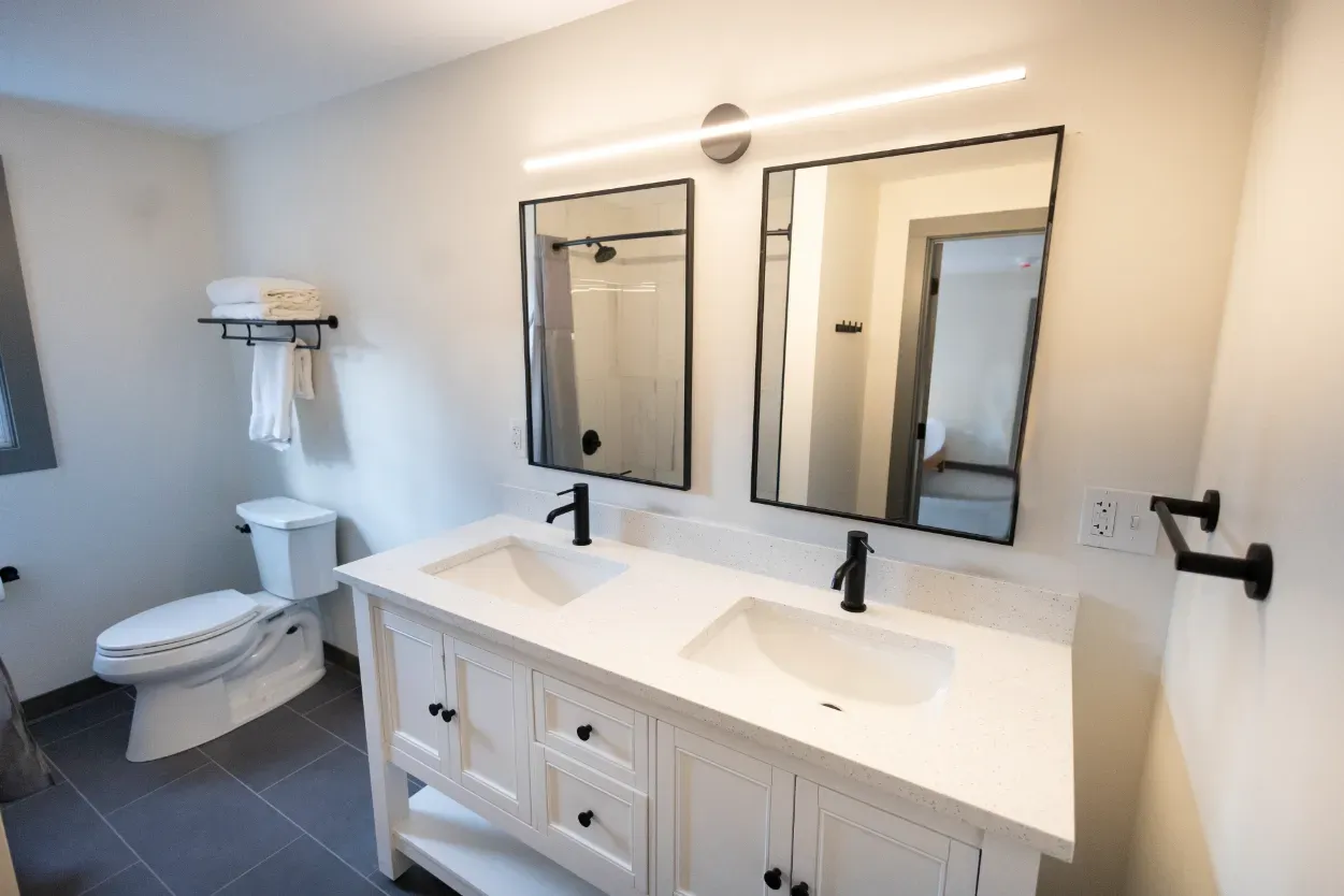 A bathroom with two sinks , a toilet and two mirrors.