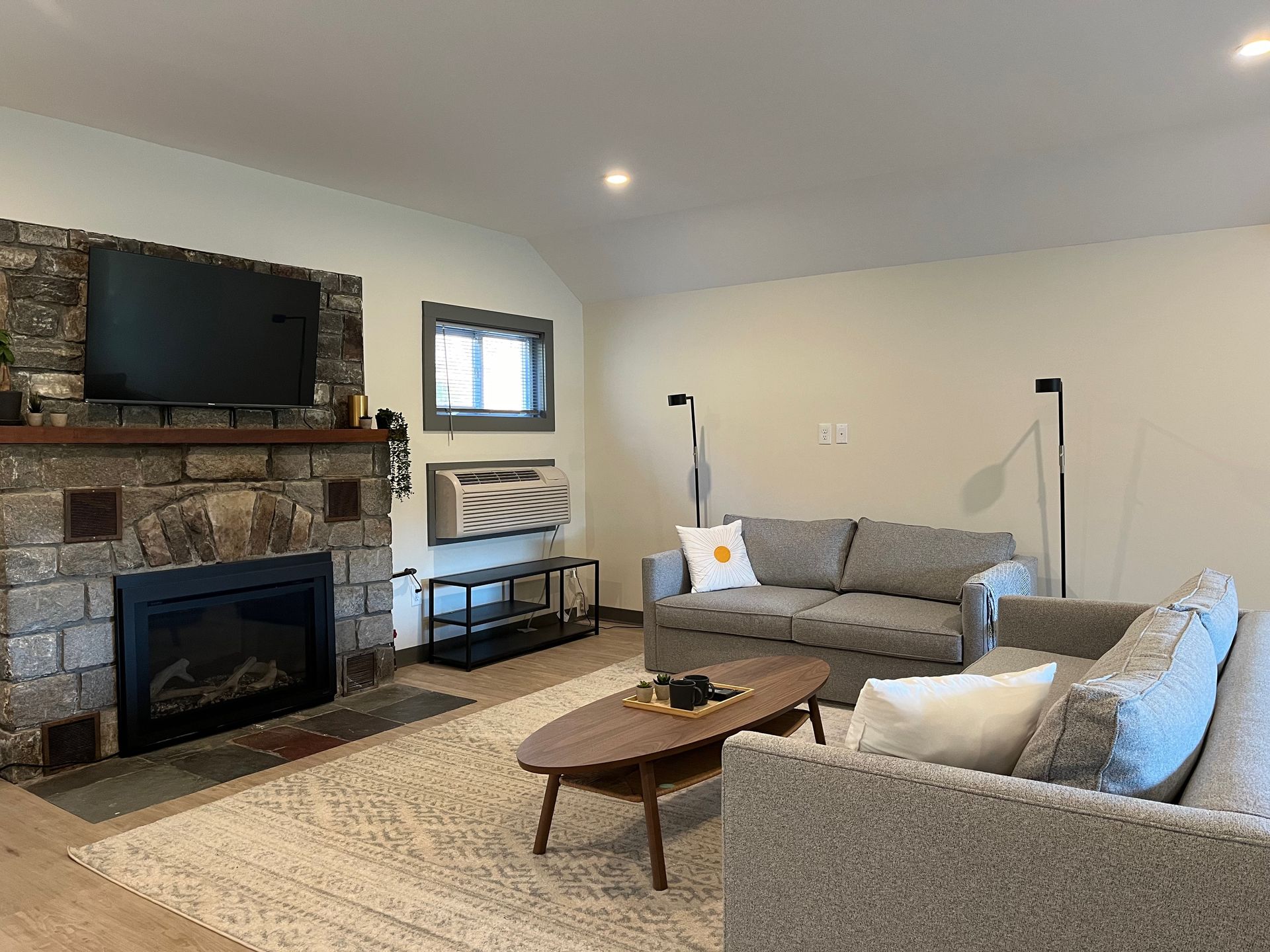 A living room with a couch , fireplace , television and air conditioner.