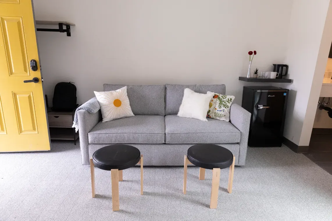 A living room with a couch , two stools and a yellow door.