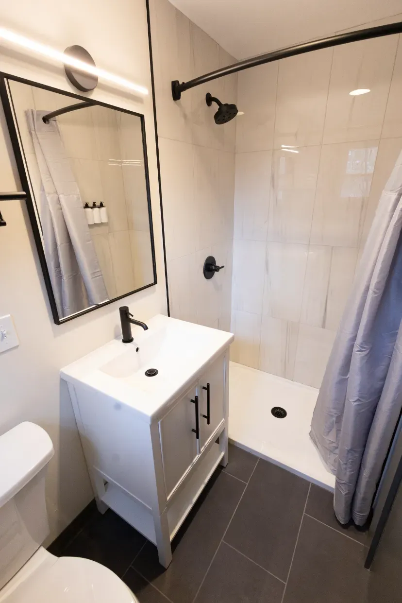 A bathroom with a toilet , sink , mirror and shower.