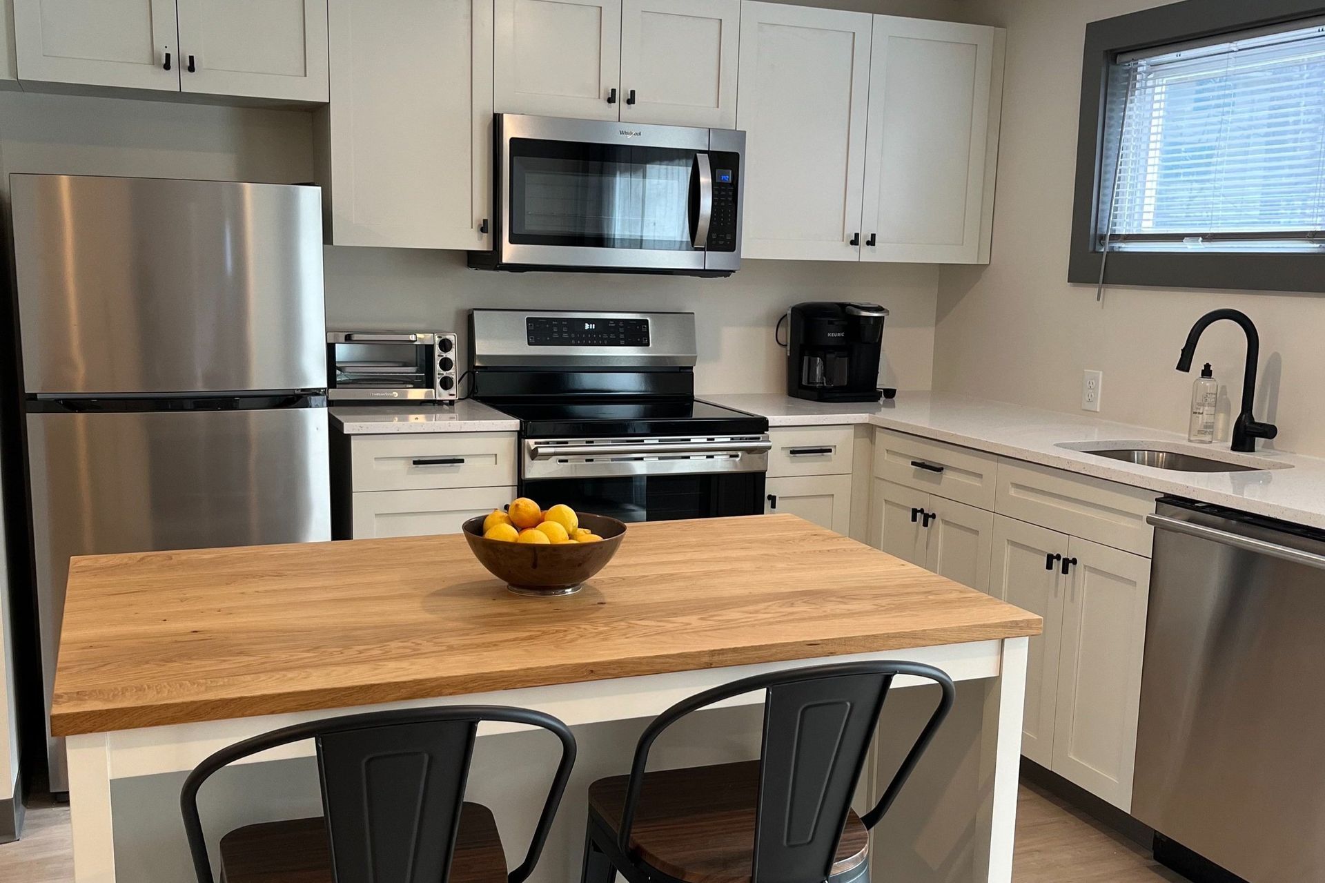 A kitchen with stainless steel appliances and a wooden table with a bowl of lemons on it.
