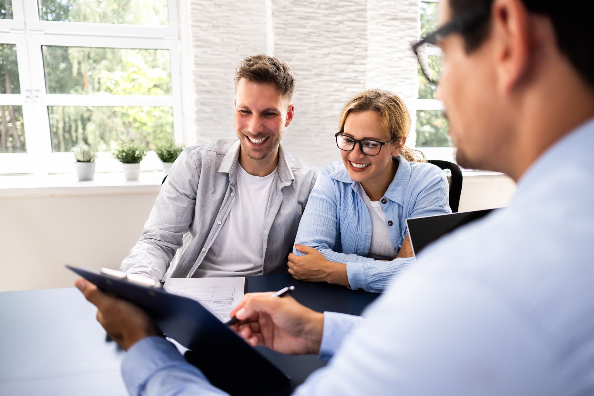 Couple smiles while looking at a tablet with a consultant in an office.